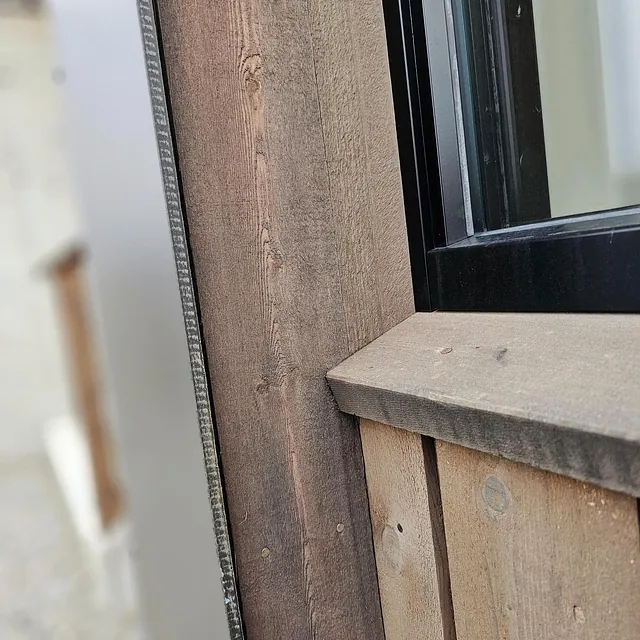 Nærbilde av vindusinnramming med ubehandlet kledning i tre.